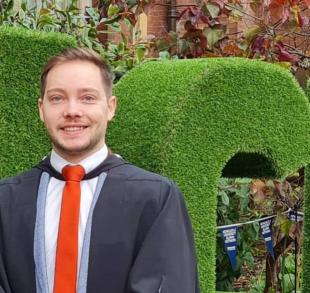 Andrew Russell on graduation day, headshot with green hedge in background