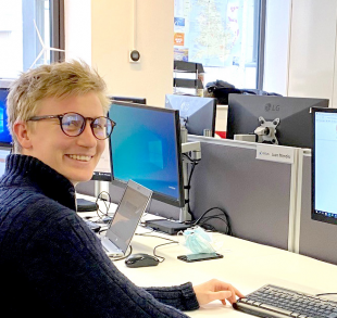 Ben sitting at a desk with computer looking back over his shoulder, smiling