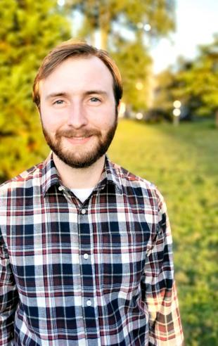 Photograph of Calum Dunnett from waist up wearing check shirt with grass and trees in background