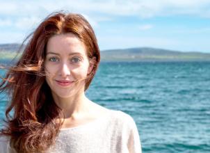 Alyona Naberezhnykh headshot with sea mountains and blue sky in the background