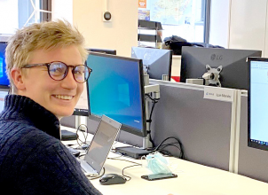 Ben sitting at a desk with computer looking back over his shoulder, smiling