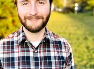 Photograph of Calum Dunnett from waist up wearing check shirt with grass and trees in background